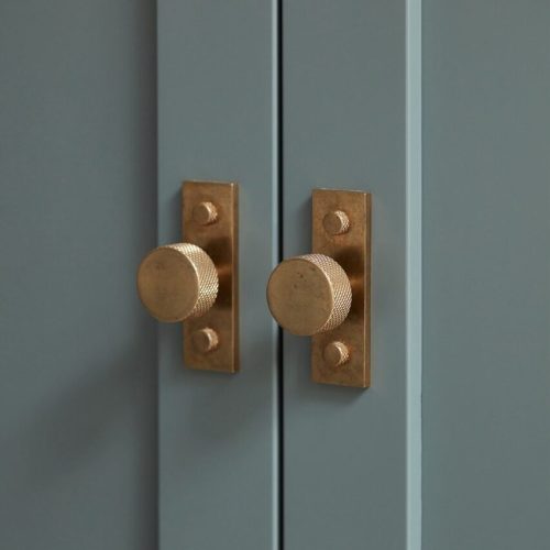Close-up of two brass door knobs with textured surfaces on a blue-gray cabinet. The knobs are mounted on rectangular backplates, reflecting a modern and elegant design.