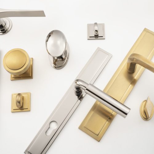 A collection of various door handles and knobs in silver and gold finishes are arranged on a white background. The designs include modern lever handles, rounded knobs, and rectangular plates.