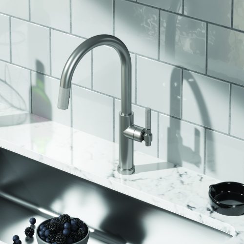 Modern kitchen sink with a sleek, curved stainless steel faucet against a white subway tile backsplash. The countertop is white marble, and there is a bowl of blackberries nearby.