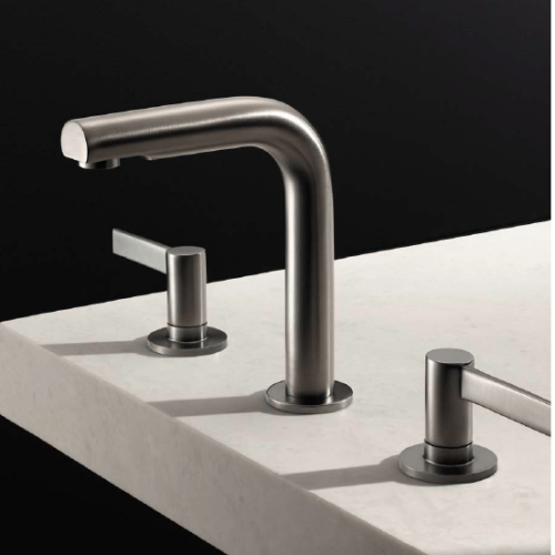 A sleek, modern stainless steel bathroom faucet set against a dark background. The faucet has a curved spout and is mounted on a light-colored countertop with two matching handles on either side.