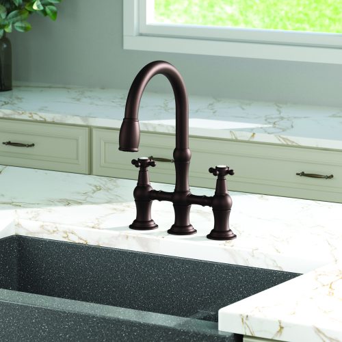 A kitchen with a dark bronze faucet featuring curved spout and dual handles, set against a white marble countertop with gold veining. Light green cabinets with silver handles are partially visible, and a window shows a grassy outdoor view.