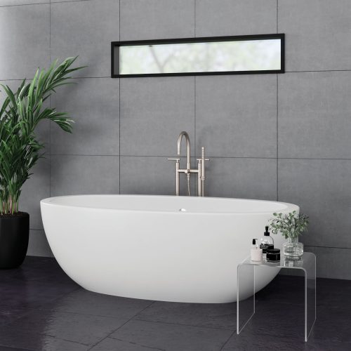 A modern bathroom features a white oval freestanding tub against gray tiled walls. A sleek metal faucet is mounted on the tub's edge. A narrow rectangular window is above, and a glass table holds toiletries. A tall potted plant is nearby.